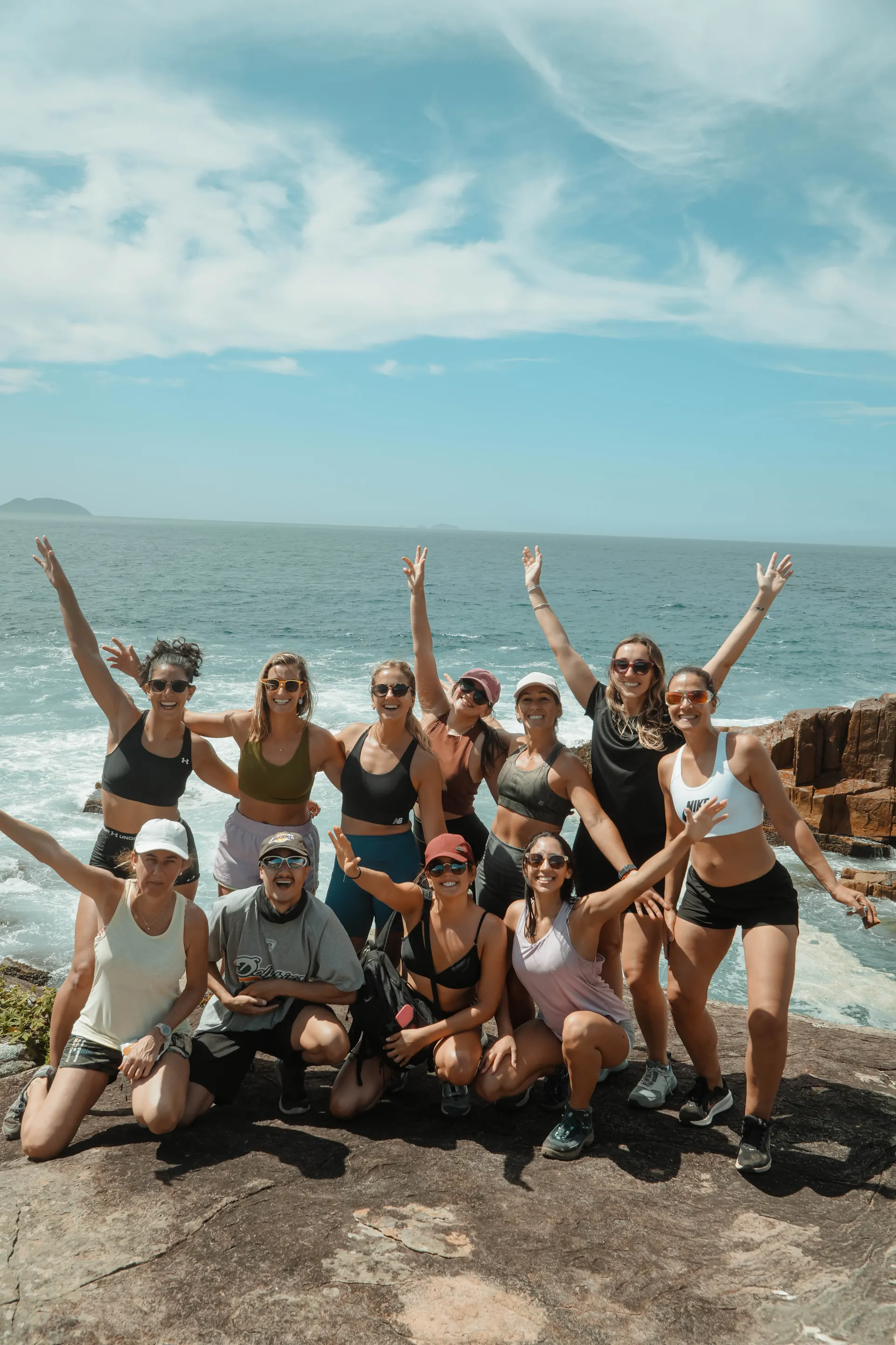 Grupo de viajeros celebrando arriba de un acantilado, mar de fondo